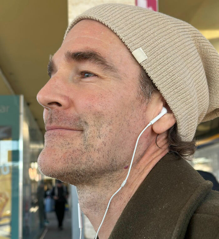 Close-up of man wearing a beige beanie and earphones, capturing an emotional moment linked to Alfonso Ribeiro and James Van Der Beek.