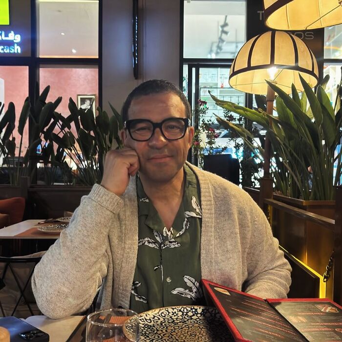 Man wearing glasses and a cardigan sitting in a restaurant, related to celebrities falsely accused of crimes.