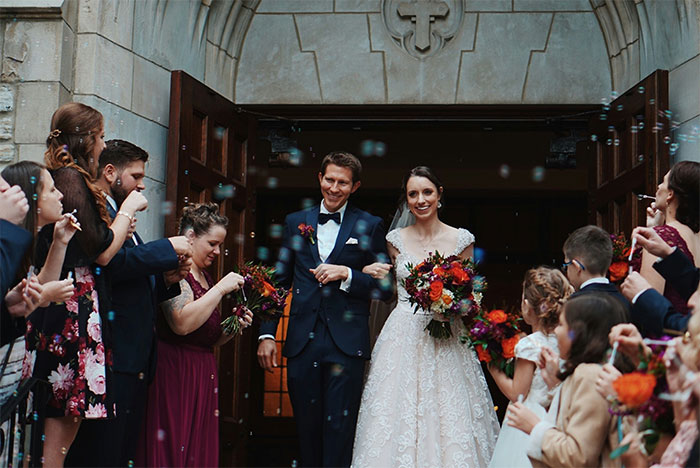 Bride and groom smiling outside church while guests celebrate, man upset about forced beer at wedding and music issues
