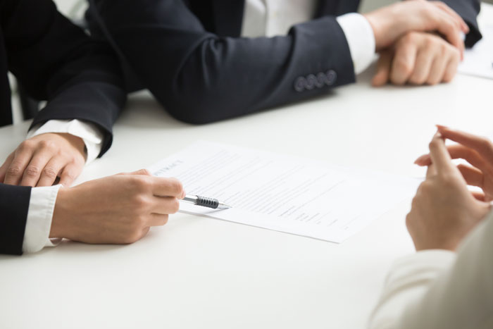 Two women in formal attire discussing inheritance documents across a white table in a serious meeting.