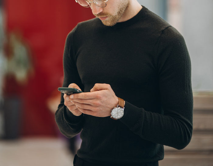 Man in black sweater using smartphone, representing concepts of wife fakes transaction to hide income source.