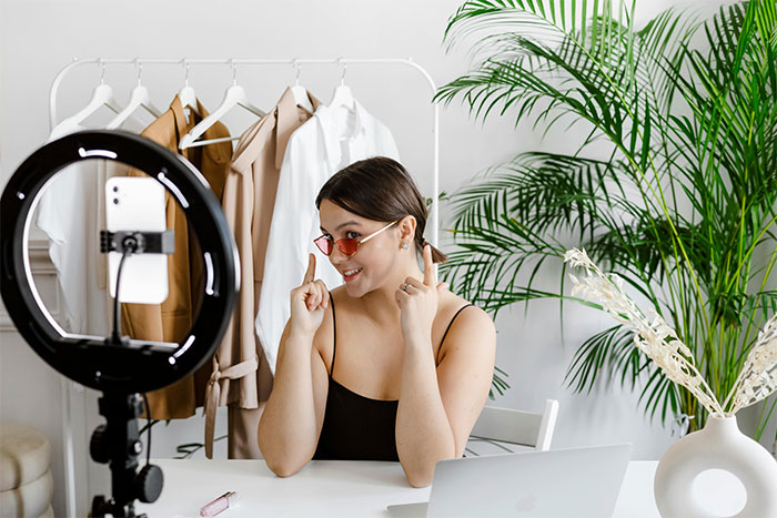 Young woman filming content with a smartphone and ring light while discussing family moving in and relationship issues.