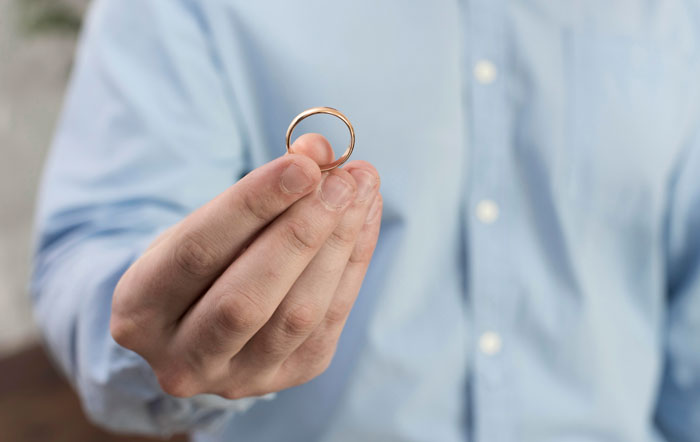 Man in blue shirt holding a wedding ring, symbolizing issues related to wife&rsquo;s secret and marital conflict.