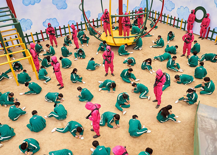 Prisoners in green tracksuits guarded by armed figures in pink suits during a dramatic scene inspired by North Korea public executions.