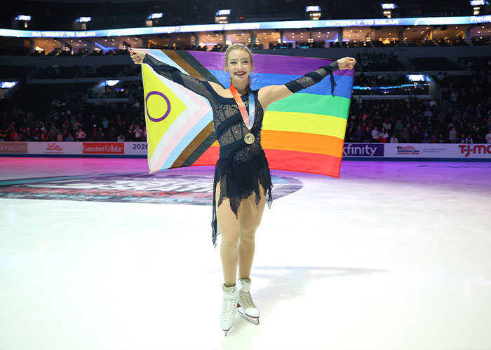 Amber Glenn on ice wearing a medal, holding a colorful pride flag symbolizing her beliefs and the backlash she faced.