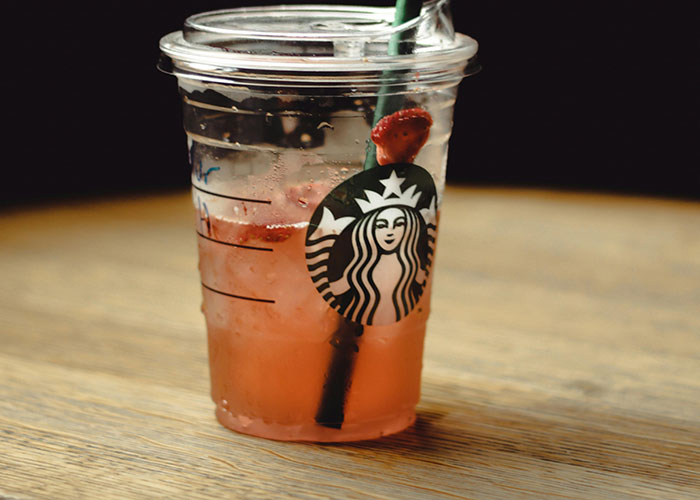 Clear plastic Starbucks cup with pink iced drink and strawberry garnish on wooden table in casual setting.