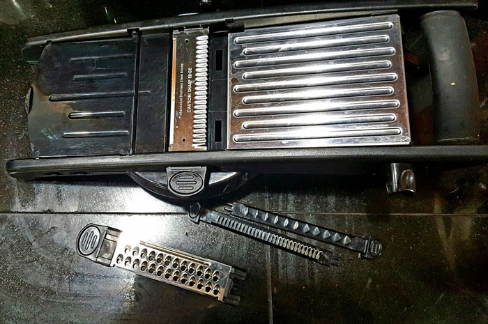 Mandoline slicer with interchangeable blades on a black surface highlighting sharp kitchen tools healthcare workers avoid using.