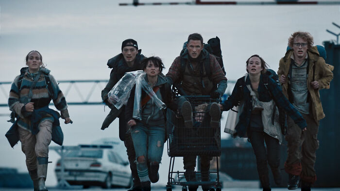 Group of young people in rugged clothing running with a shopping cart in a post-apocalyptic setting for shows like Fallout. - 5