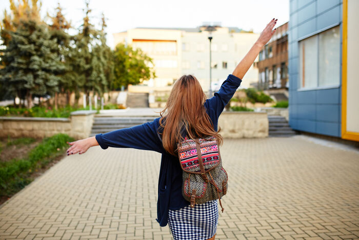Young woman with a colorful backpack walking away joyfully, symbolizing removal from a nasty situation and wake-up calls.