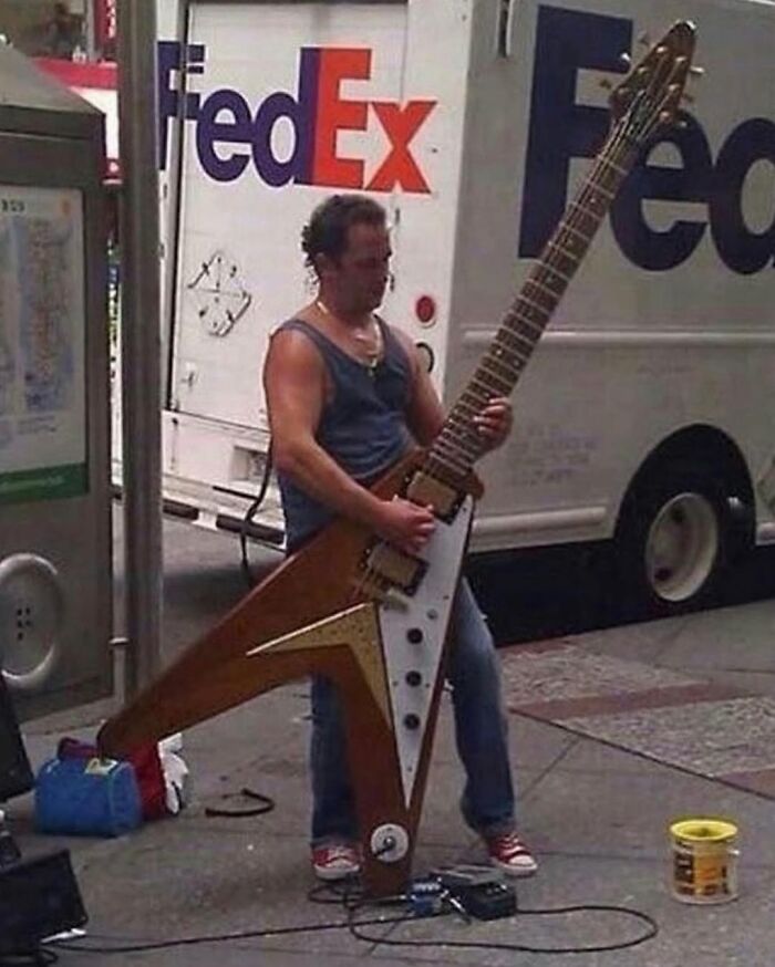 Man playing an oversized guitar on a city street, a weirdly hilarious image to boost your feed and mood.