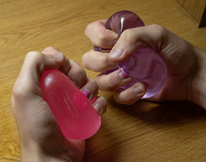 Hands squeezing red and purple stress balls on a wooden surface relating to TikTok trend injuries and facial burns.