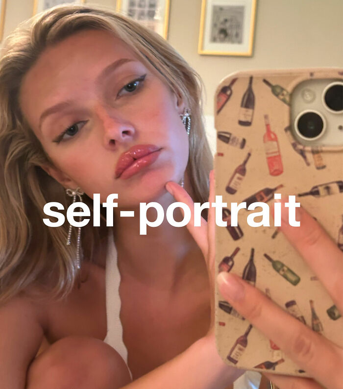 Apple Martin taking a self-portrait selfie, revealing cosmetic procedures, holding phone with wine bottle patterned case.