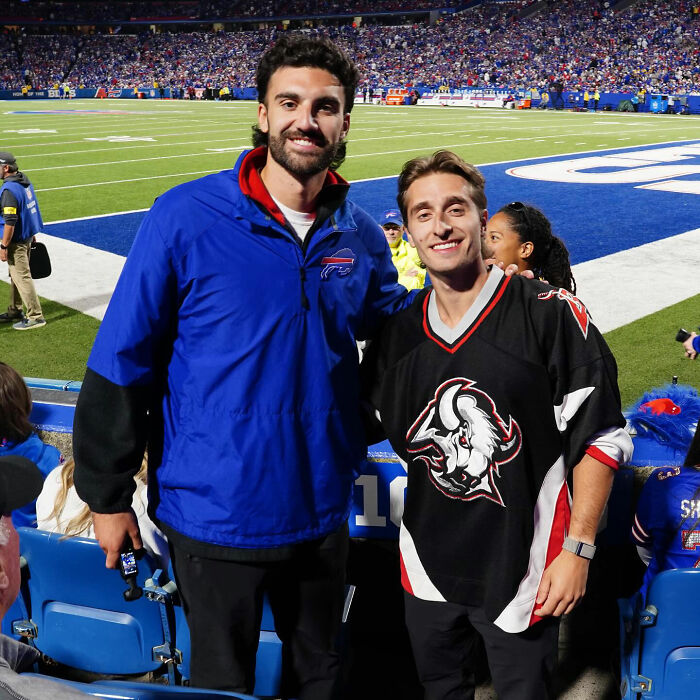 Two men smiling at a stadium wearing hockey gear, representing Canadian hockey fans and their bold Olympic bet backfiring.