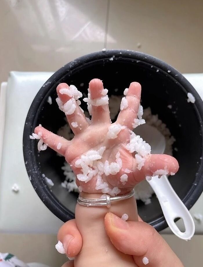 A weirdly hilarious image of a hand stuck in a rice cooker, covered with sticky rice grains.
