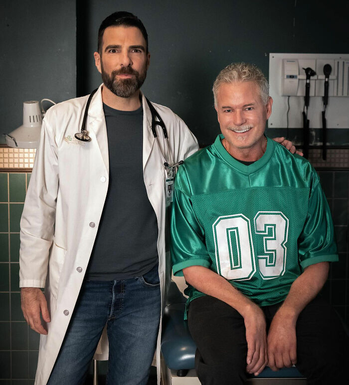 Eric Dane smiling in a green jersey with a man in a white coat and stethoscope in a medical setting.