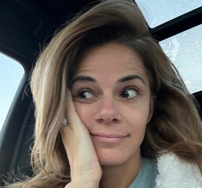 Woman with long hair resting her face on her hand inside a car, relating to influencer claps back and hotel hack controversy.