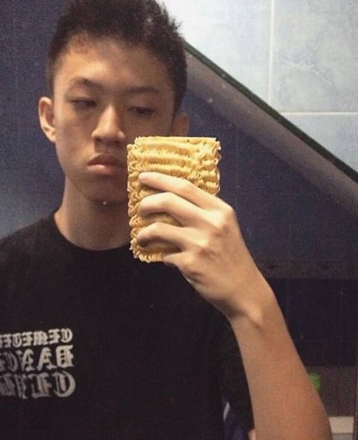 Young man taking a selfie with a rectangular block of uncooked instant noodles as his phone case in a weirdly hilarious image.