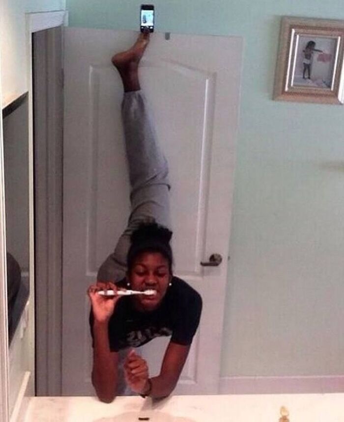 Woman brushing teeth upside down using foot to hold phone for a weirdly hilarious image to improve your feed and mood.