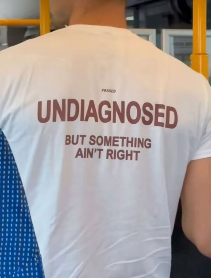 Person wearing a white shirt with funny text reading undiagnosed but something ain’t right in a public transit setting weirdly hilarious image