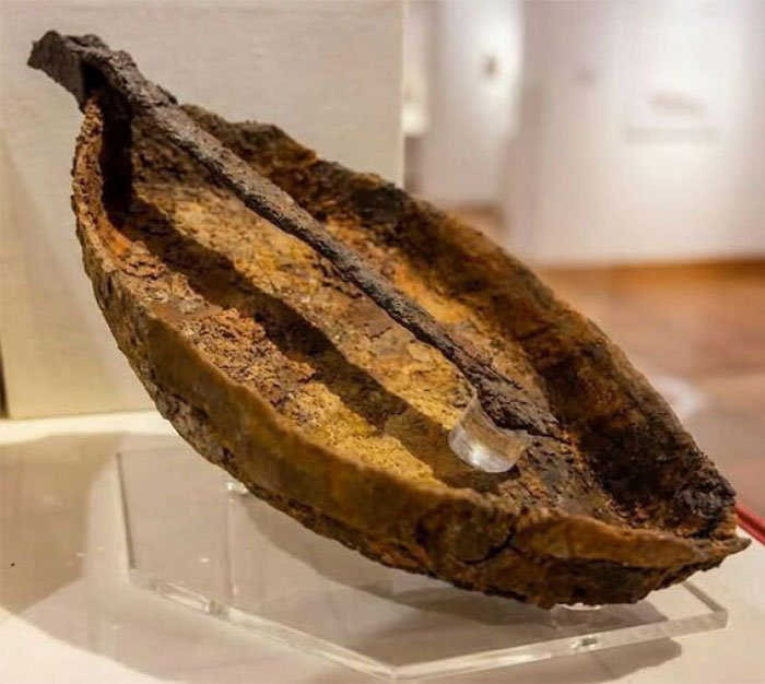 Rusty ancient historical artifact displayed on a clear stand in a museum of artifacts with blurred background.