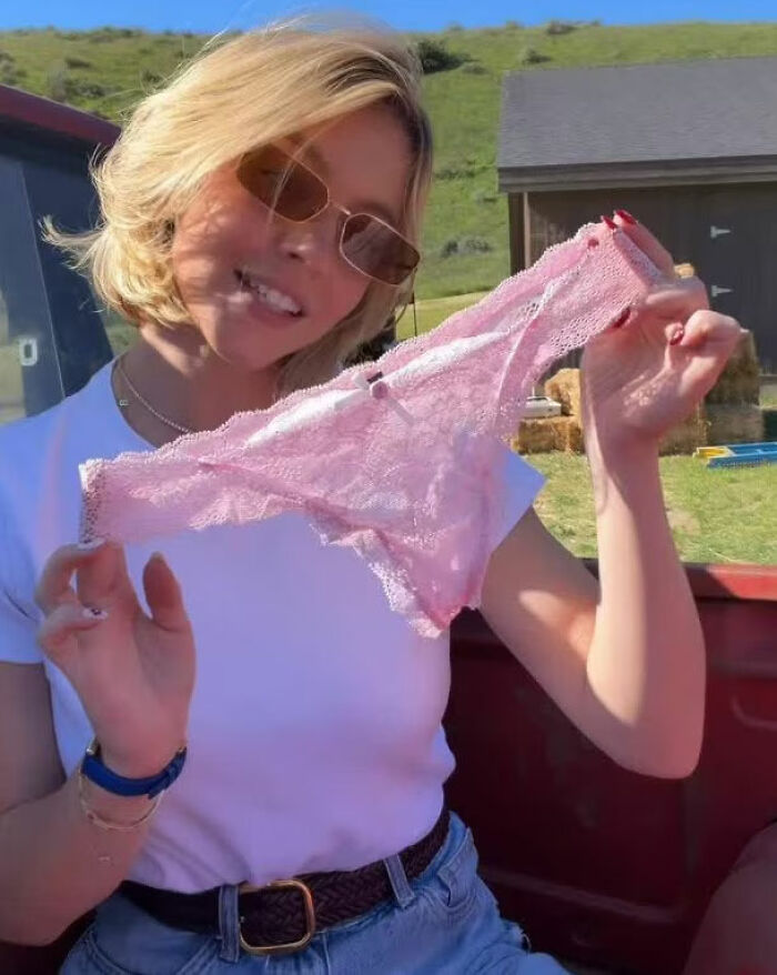 Sydney Sweeney posing outdoors holding pink lace lingerie in a casual setting for marketing promo campaign.