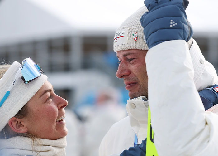 Olympic medalist emotional and tearful after victory, facing a woman in winter sports gear during celebration.