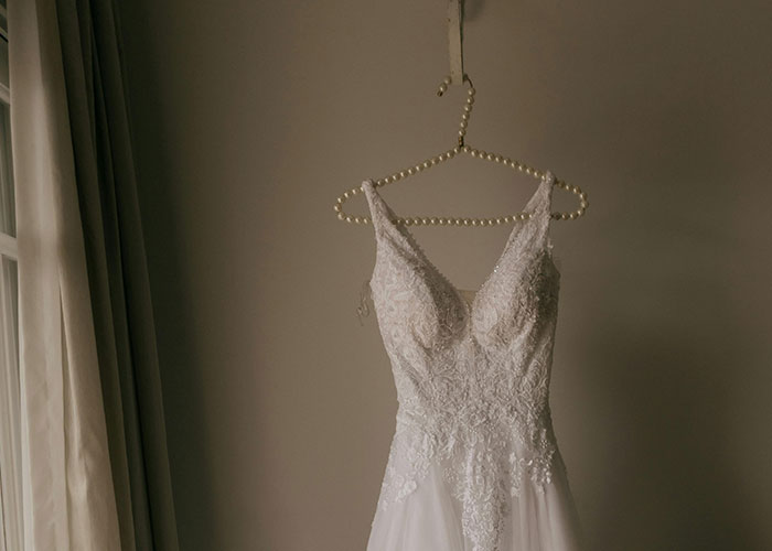 Wedding dress hanging on a pearl hanger in a softly lit room, symbolizing a stepmom's wedding day conflict.
