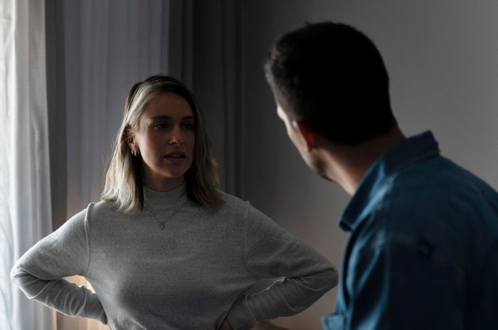 Wife fakes transaction and confronts husband in a dimly lit room about hiding income source during a serious discussion.