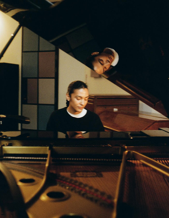Olivia Dean playing piano in a cozy room with her reflection visible on the piano lid, showcasing Best New Artist.