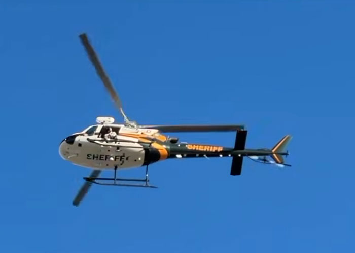 Helicopter with sheriff markings flying in clear blue sky, linked to hostage negotiator chilling new theory.