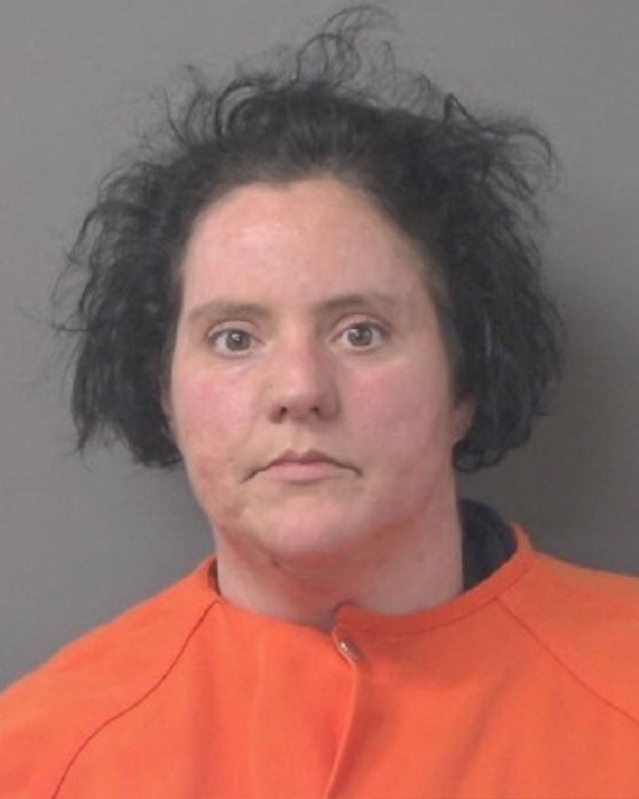 Mugshot of a vet tech wearing an orange jumpsuit after rescuing an abandoned dog during a snowstorm.