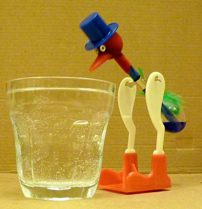 Toy bird with top hat dipping beak into glass of sparkling water, a quick fix turned out to be genius idea.