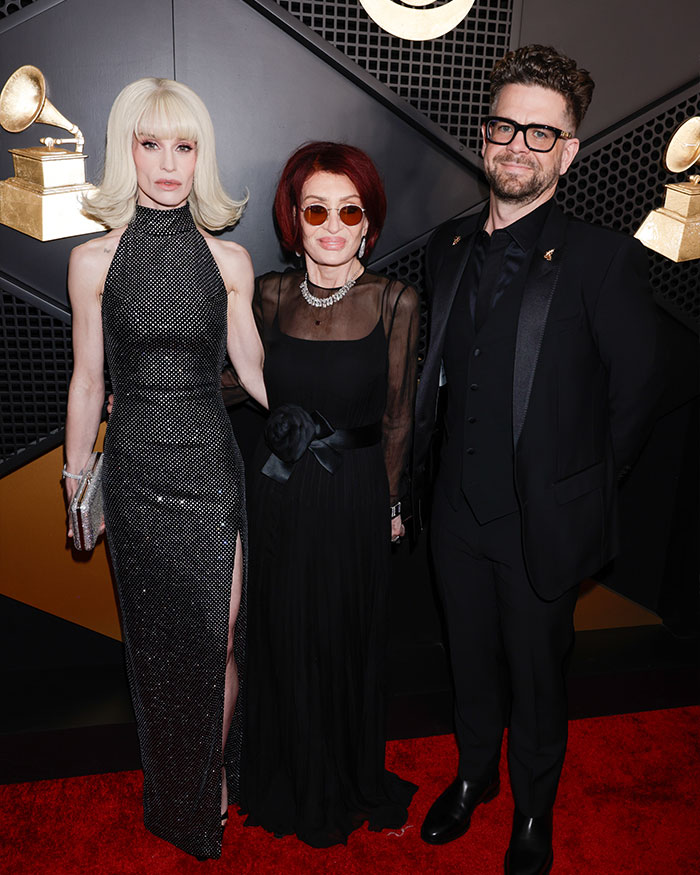 Kelly Osbourne with two guests on the red carpet wearing elegant black outfits at a Hollywood event.
