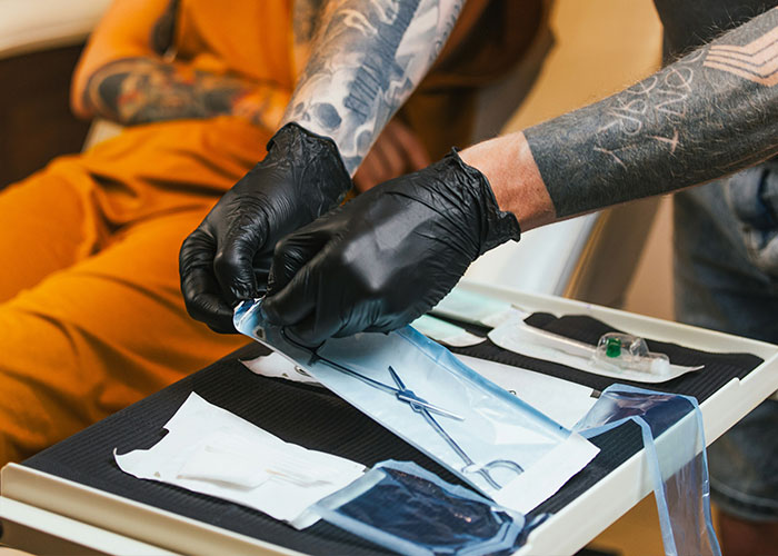 Tattoo artist wearing black gloves preparing sterile tools for a procedure, highlighting health experts' concerns on viral looks.
