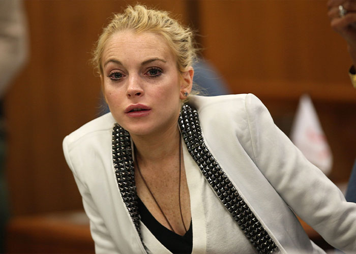 Lindsay Lohan wearing a white jacket, speaking candidly about the dark side of growing up famous in an interview.