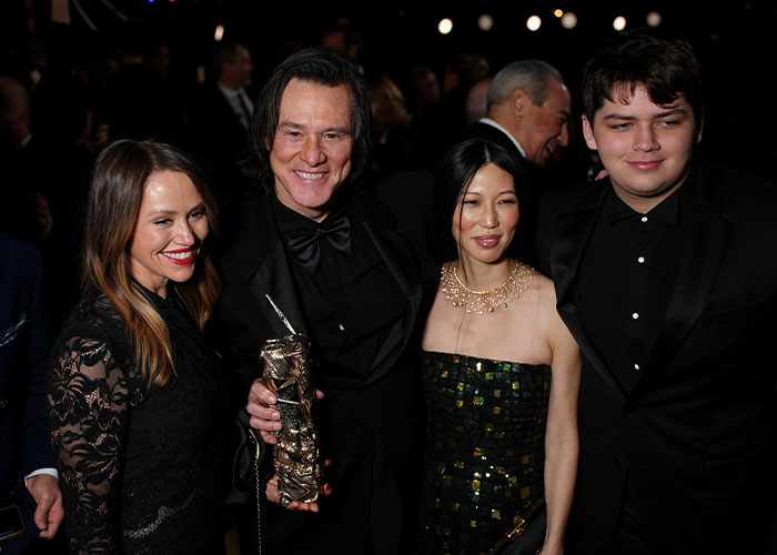 Jim Carrey holding an award, smiling with three people at a formal event, fans discussing viral footage reactions.