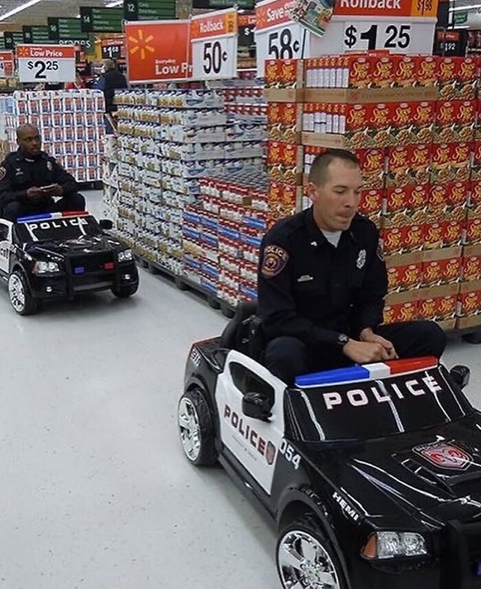 Two police officers riding in toy police cars inside a grocery store aisle in a weirdly hilarious scene.