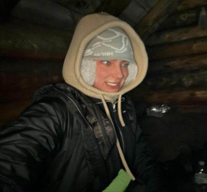 Young woman hiking New York's highest peak with her dog, dressed warmly in a black jacket and hooded hat indoors.