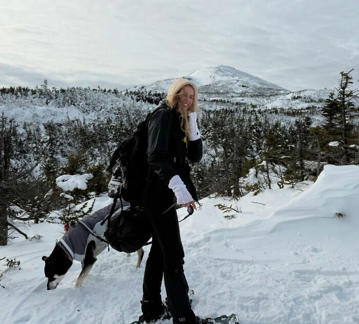 Young woman hiking New York's highest peak with her dog in snowy conditions, surrounded by winter trees and mountain scenery.