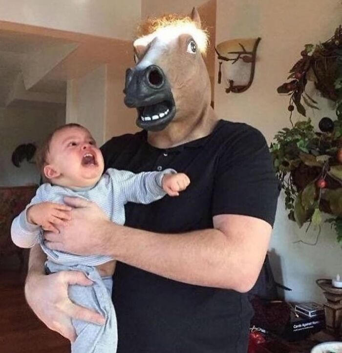 Person wearing a horse mask holding a crying baby, a weirdly hilarious image to improve your mood and feed.