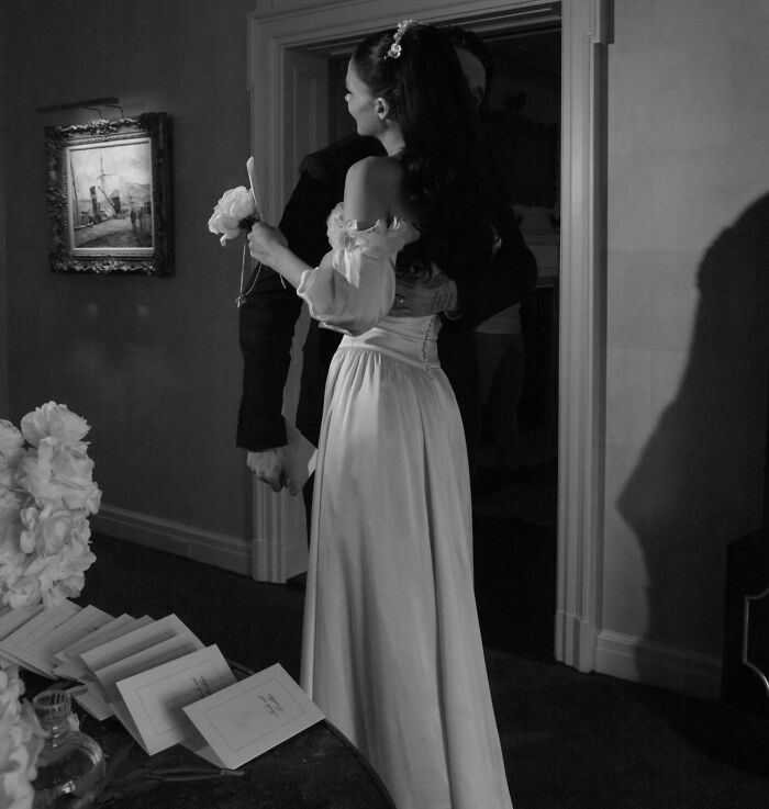 Couple embracing indoors near table with wedding invitations, related to Marc Anthony and Brooklyn Beckham wedding accusations.
