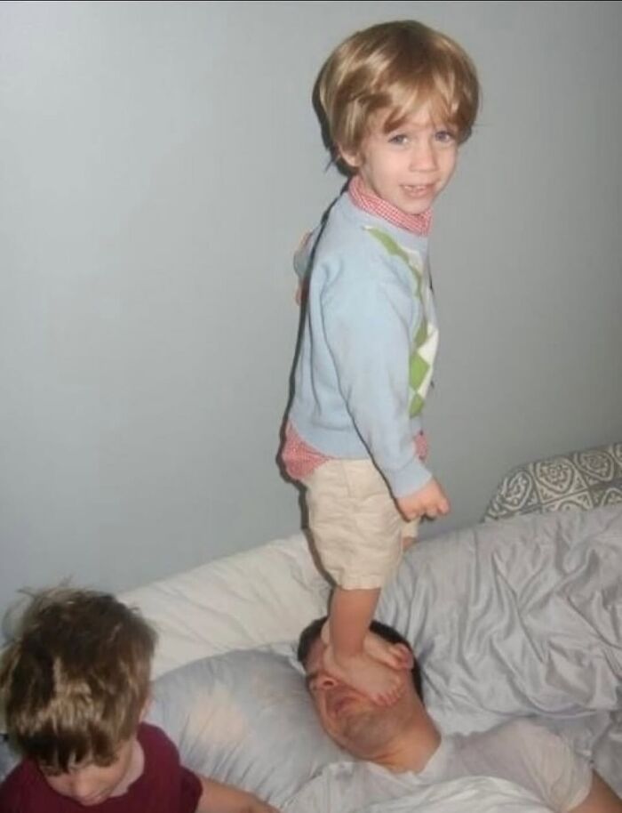 Child standing on a man's face while another kid sits nearby, a weirdly hilarious image to lighten your mood.