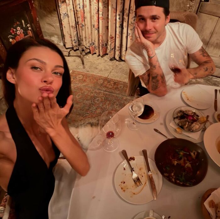 Couple enjoying dinner at a table with empty plates and wine glasses, related to Marc Anthony Brooklyn Beckham wedding news.