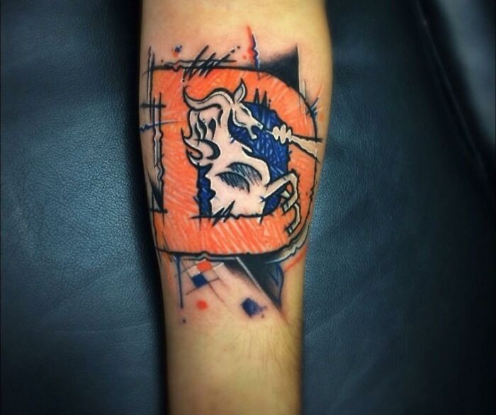 Abstract Denver Broncos tattoo on forearm with distorted design and rough black outlines, showcasing bad tattoos with unusual art style.
