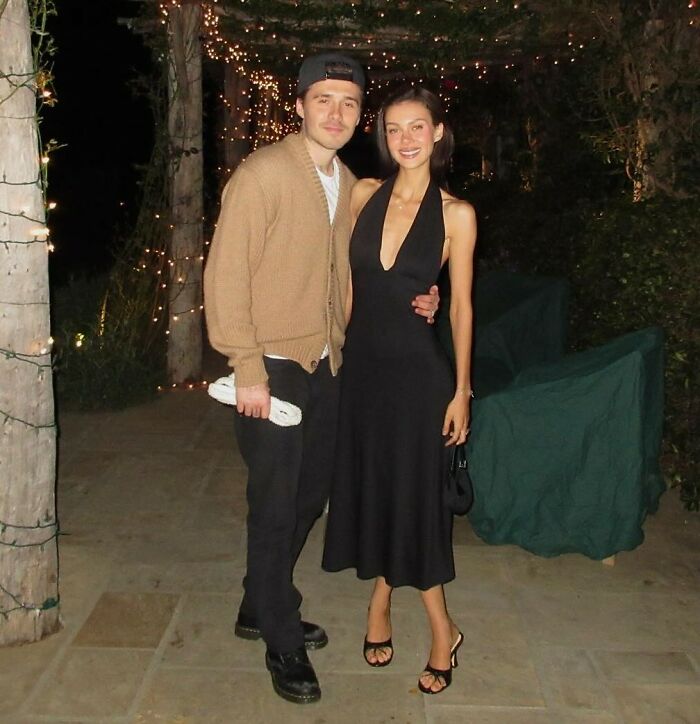 Marc Anthony and woman posing outdoors at night with string lights, related to Brooklyn Beckham wedding accusations.
