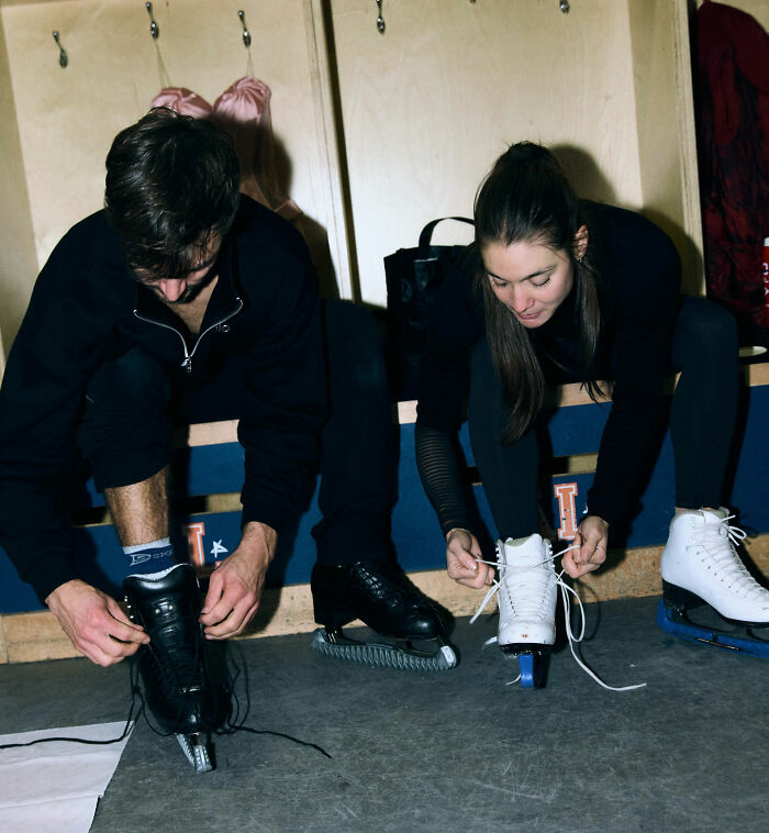 Two figure skaters sitting on a bench lacing up skates, representing US figure skating after cheating scandal impact.
