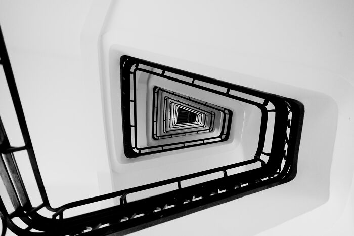 An example of unreal architecture: a high-angle, black and white shot looking down a triangular, geometric spiral staircase.