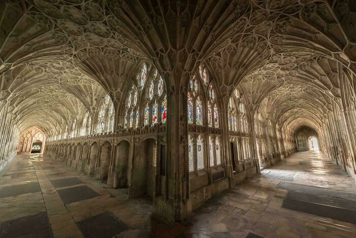 Beautiful architecture featuring a long, arched stone hallway with detailed ceilings and stained glass windows, evoking a sense of history.