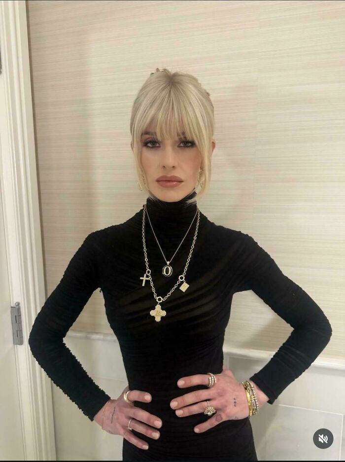 A woman in a black turtleneck and multiple necklaces strikes an unnatural pose for social media.