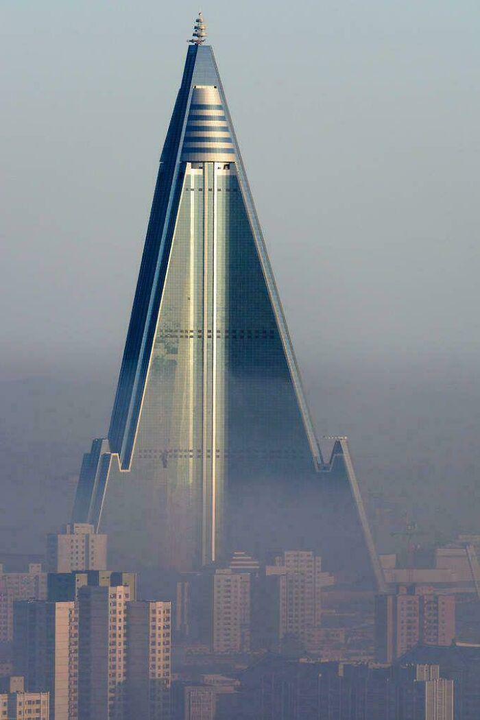 A triangular, skyscraper building rising through the fog, resembling a structure for an evil mastermind.
